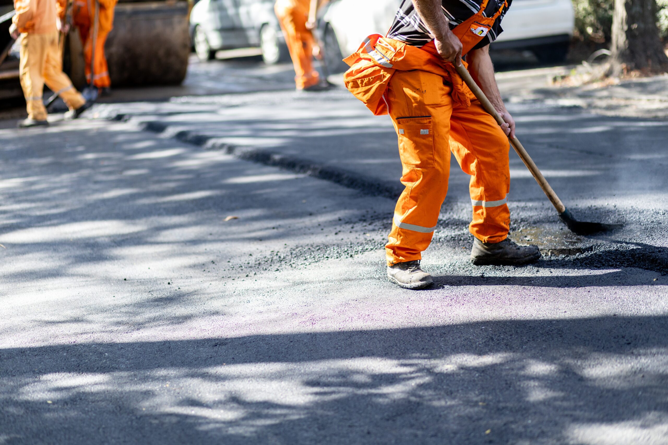 Construction,Workers,In,Bright,Orange,Attire,Are,Smoothing,Asphalt,On